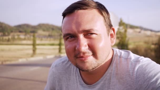 Chubby pleasant man looks in cameo and smiles against the background of the road and trees - Séquence, vidéo