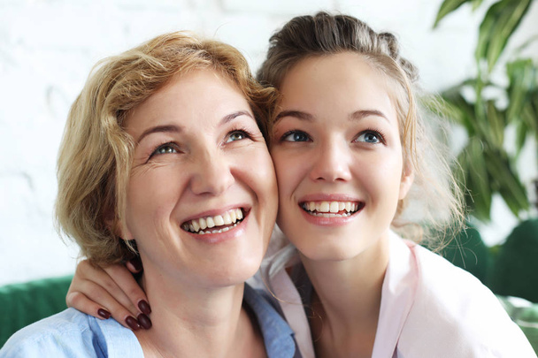 Beautiful senior mom and her adult daughter are hugging, looking at camera and smiling. At Home. - Photo, Image