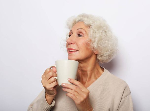 old excited lady smiling laughing, holding cup drinking coffee, tea, over white background - Фото, изображение