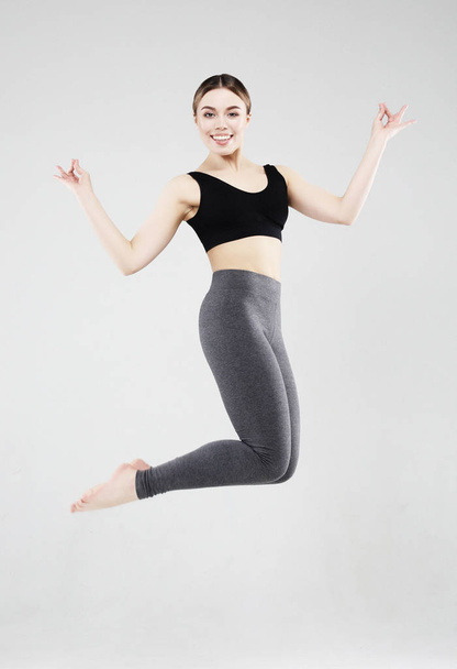 Sport, fitness and people concept: Beautiful young woman dressed in sportswear jumping up over grey background - 写真・画像