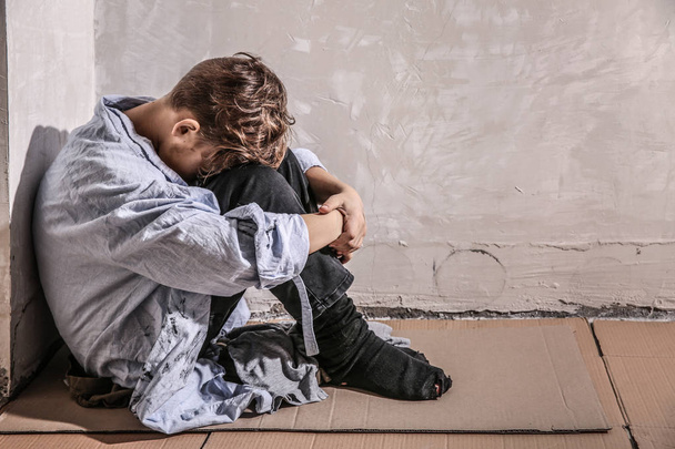 Бездомний маленький хлопчик сидить на підлозі біля стіни
 - Фото, зображення