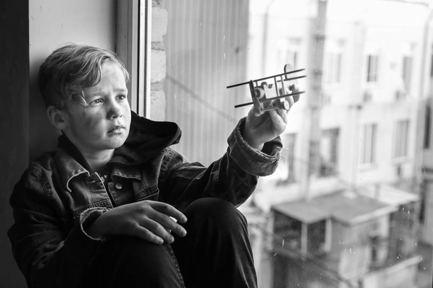 Piccolo ragazzo senzatetto che gioca con l'aeroplano vicino alla finestra al chiuso
 - Foto, immagini