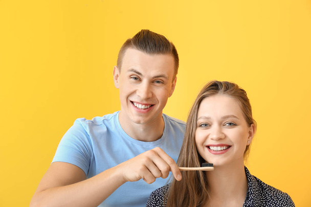 Щасливий чоловік допомагає своїй дівчині чистити зуби на кольоровому фоні
 - Фото, зображення