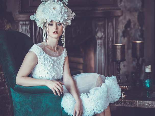 Beautiful young bride wearing white dress and wreath of flowers sits on a chair. Luxury palace. - Foto, Imagem