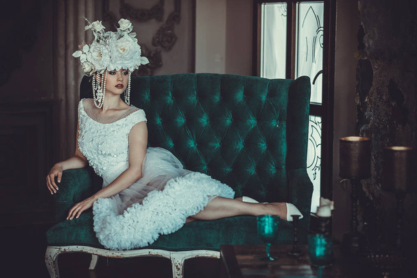 Beautiful young bride wearing white dress and wreath of flowers sits on a chair. Luxury palace. - Fotoğraf, Görsel