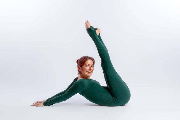 Beautiful slim woman in sports overalls  doing yoga, standing in an asana balancing pose - posture connection  on white  isolated background. The concept of sports and meditation. Training for stretching and yoga - Photo, Image