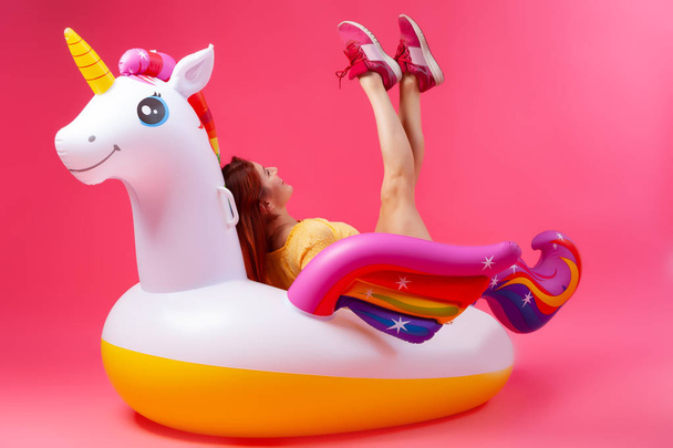 Yaz moda güzel kadın yaz giysileri eğlenmek, gülümseme ve balon ile poz üzerinde Unicorn float izole pembe arka plan - Fotoğraf, Görsel