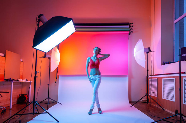Backstage: model woman with in underwear,  jeans posing in attractive position in colorful bright neon yellow and pink lights in studio. Fashion concept - Photo, Image