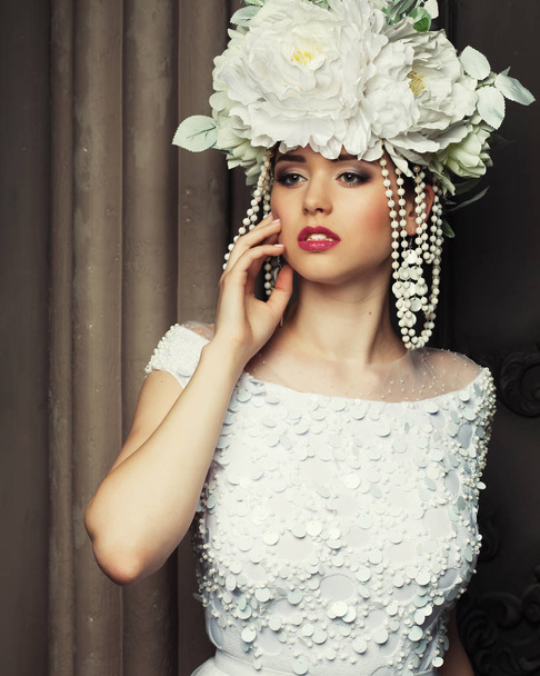 Young beautiful woman wearing white dress and wreath of flowers standing in the palace room. - Foto, afbeelding