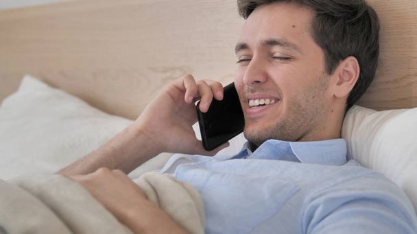 Relaxing Young Man Talking on Phone in Bed - Photo, Image