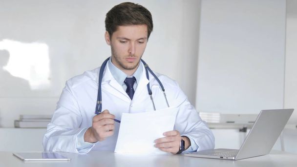 Médico jovem que lê o relatório médico, fazendo a papelada
 - Foto, Imagem