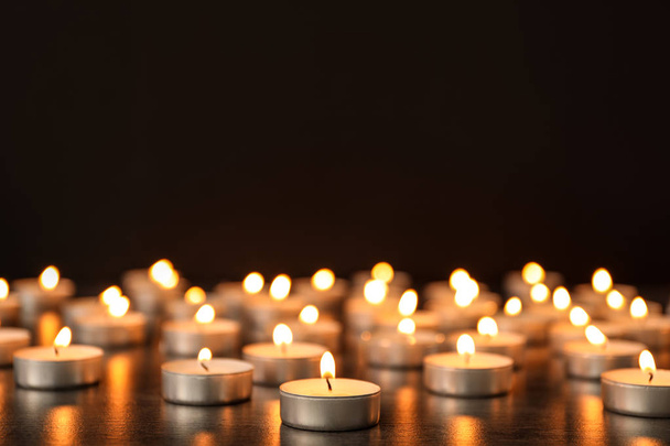 Many burning candles on table against dark background. Symbol of sorrow - Foto, afbeelding