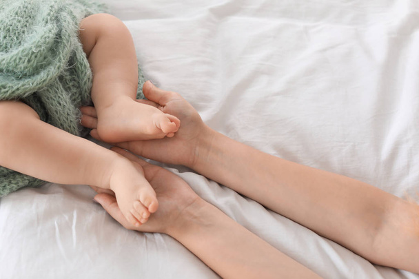 Mother holding feet of her little baby on bed, closeup - Foto, imagen