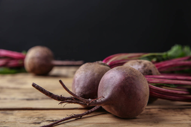 Fresh beets with leaves on wooden table against black background, closeup. Space for text - Foto, afbeelding