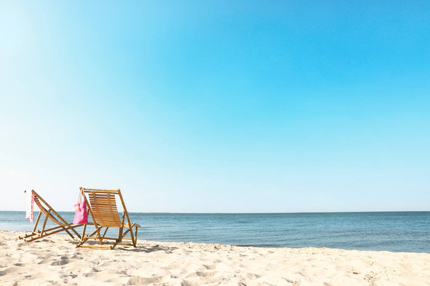 Empty wooden sunbeds and beach accessories on sandy shore - Valokuva, kuva