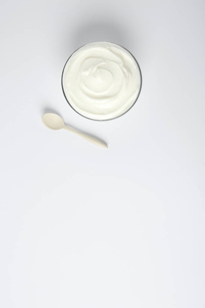 Glass bowl of sour cream and spoon on white background, top view - Fotoğraf, Görsel