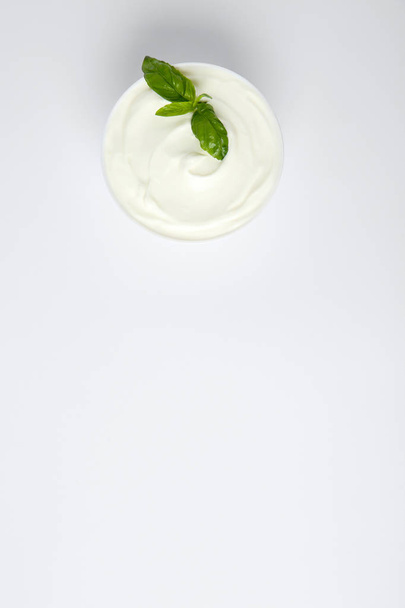Bowl of fresh sour cream with basil on white background, top view - 写真・画像