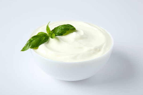 Bowl of fresh sour cream with basil on white background - Fotoğraf, Görsel