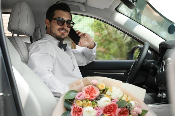 Joven hombre guapo con hermoso ramo de flores sentado en el coche
 - Foto, Imagen