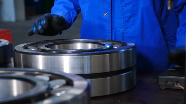Machinery and industry concept. Set of various gears and ball large bearings, spare parts warehouse. Male worker hands in blue uniform in bearing factory. A qualified employee at plant putiing large - Footage, Video