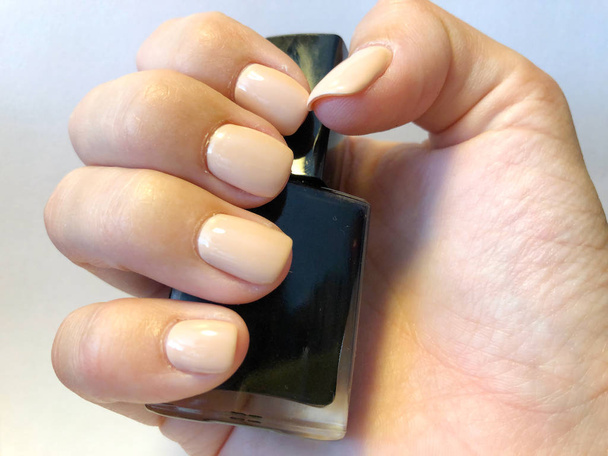 Женские руки держат лак для ногтей голым. Крупным планом пальцы с маникюром
 - Фото, изображение