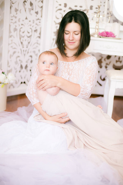 Young mom with a baby in her arms in the bright boudoir bedroom - Фото, зображення