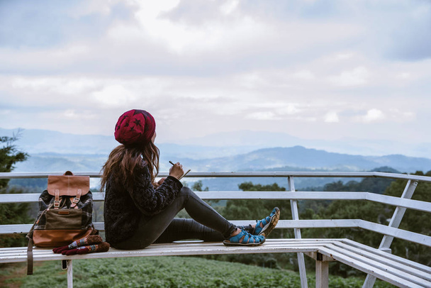 The girl is sitting relaxing at the natural mountain viewpoint and writing a record of her winter travel. smiled happy writing a diary. - Photo, Image