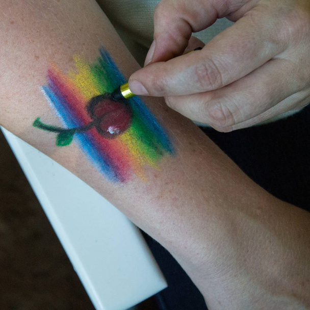 Rainbow and cherry painted face painting on a human hand - Φωτογραφία, εικόνα