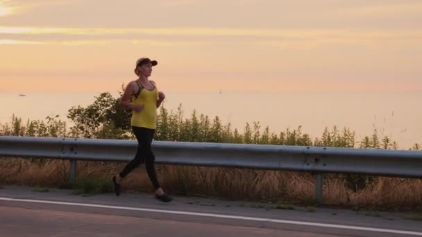 Mujer hace una tarde trote a lo largo de la carretera a lo largo del lago
 - Metraje, vídeo