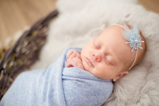 Τέλειο νεογέννητο μωρό κορίτσι σε μπλε κουβέρτα σε ένα ψάθινο καλάθι διακοσμημένο με κλαδιά από άνθη κεράσι άνοιξη - Φωτογραφία, εικόνα
