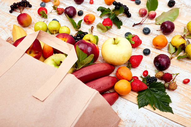 Χάρτινη σακούλα με διάφορα φρούτα της υγείας τροφή σε ξύλινο φόντο. Κορυφαία προβολή. Επίπεδη, μπεζ καραβόπανο τσάντα παντοπωλείου έπεσε πάνω ενώ πέφτουν τα φρούτα - Φωτογραφία, εικόνα