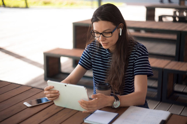 Girl, student, using the tablet, working online, using voice messages. Near notebook, a smartphone, wireless headphones. - Fotó, kép