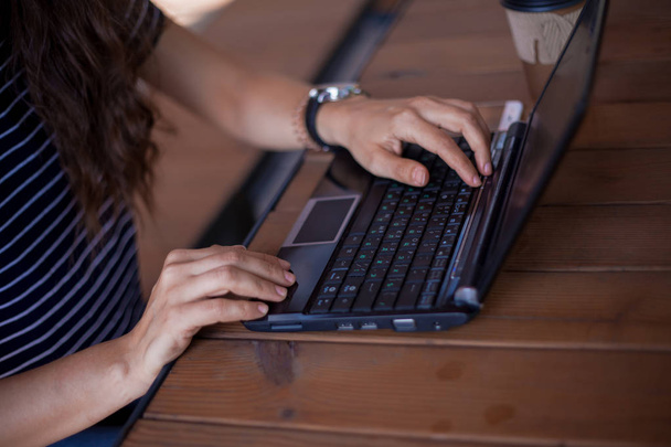 Schludne kobiece ręce bez manicure, z dużymi zegarkami na rękę, smartphone checkeng, laptop stojący na drewnianym stole. - Zdjęcie, obraz