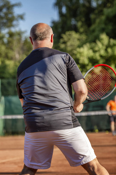 Adult bald man plays tennis on the court. Sunny day.  - Foto, afbeelding