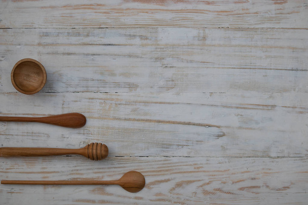 Φιλικό προς το περιβάλλον ξύλινο μπολ, κουτάλια και μέλι ραβδί σε ξύλινο φόντο τραπέζι. Φιλικό προς το περιβάλλον μαγειρικά σκεύη επίπεδη θέση με αντίγραφο χώρου. - Φωτογραφία, εικόνα