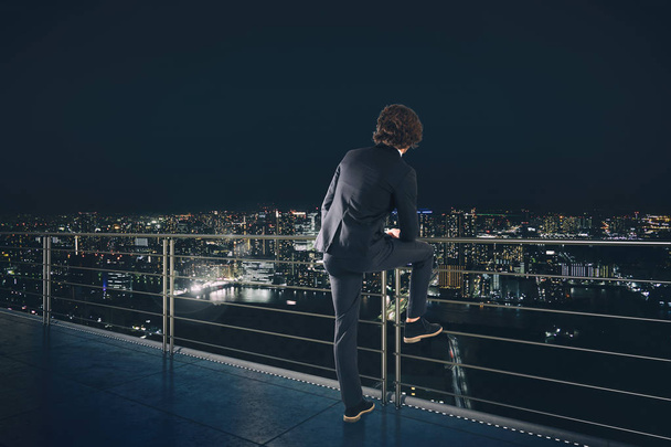 Ο επιχειρηματίας κοιτάζει την πόλη κατά τη διάρκεια της νύχτας. Έννοια του μέλλοντος και της νέας επιχειρηματικής ευκαιρίας - Φωτογραφία, εικόνα