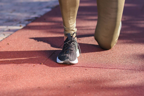 Женщина в кроссовках и спортивной одежде делает спортивные упражнения на спортивном поле, размытый фон
 - Фото, изображение