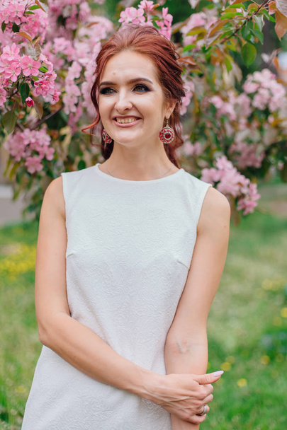 Charming woman wearing beautiful white dress standing next the pink apple tree - Fotografie, Obrázek