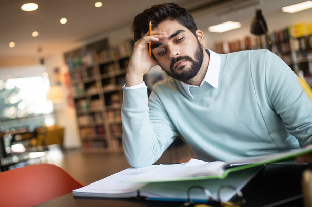 Jeune homme épuisé étudiant dans une bibliothèque universitaire
 - Photo, image