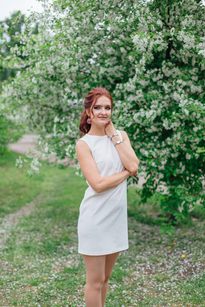 Charming woman wearing beautiful white dress standing under the apple tree - Foto, afbeelding