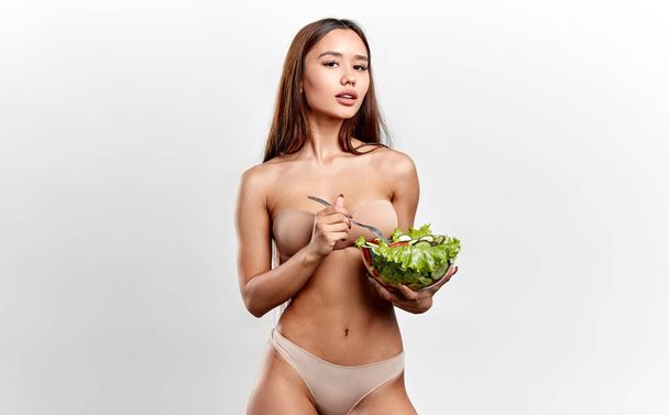 pleasant Asian sportswoman eating salad after training - Foto, afbeelding