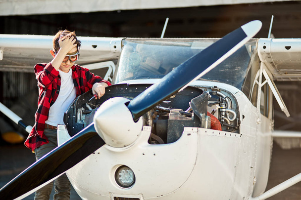boy with screwdriver looking with concern at airplane engine, trying to repair it - Foto, afbeelding