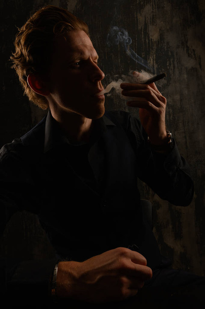 Confident casual young man and smoking cigarette. Studio portrait against dark background. - 写真・画像