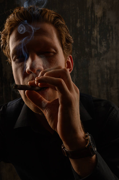 Confident casual young man and smoking cigarette. Studio portrait against dark background. - 写真・画像