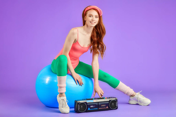 young female trainer sits on fit ball and press button on portable cassette player - Foto, immagini