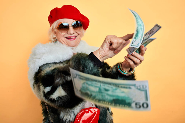 rich elegant woman in fur coat and red cap throwing money - Photo, image