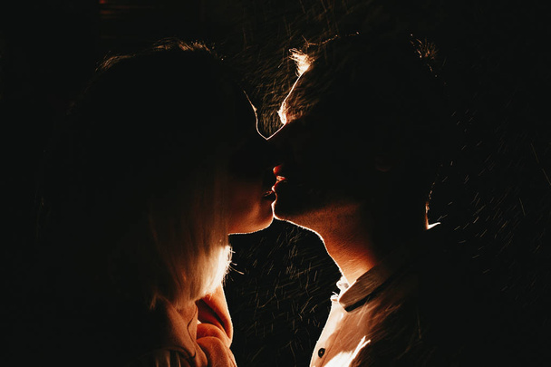 雨の中で夜にキスする恋の若い幸せなカップルのシルエット。フラッシュ効果を持つ写真 - 写真・画像