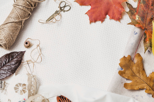 Scissors, thread and fallen leaves lie on white cloth - Φωτογραφία, εικόνα