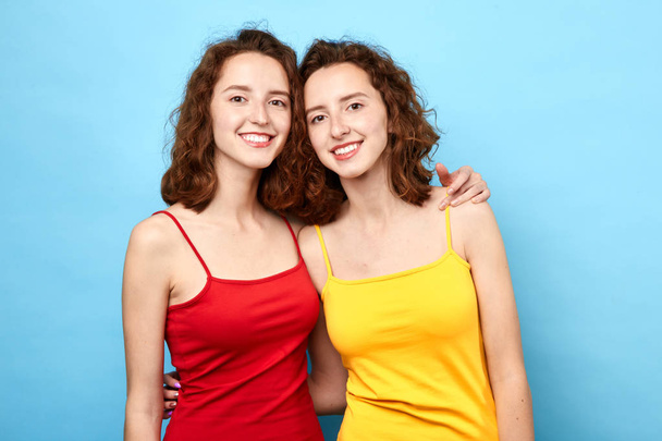 two beautiful positive sisters with wavy hair hugging and posing to the camera - Foto, afbeelding