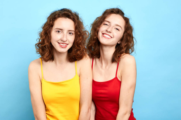 smiling twin sisters posing to the camera isolated on blue - Φωτογραφία, εικόνα